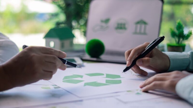 Réunion de conception durable avec des documents portant le symbole du recyclage et un ordinateur affichant des icônes écologiques