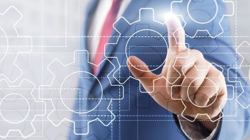 Homme daffaires en costume appuyant sur une interface numérique affichant des engrenages symbolisant lautomatisation et la transformation digitale