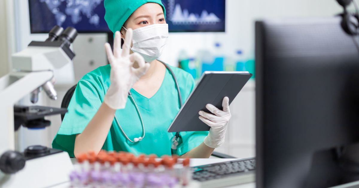 Médecin en blouse verte effectuant une téléconsultation via une tablette dans un laboratoire médical
