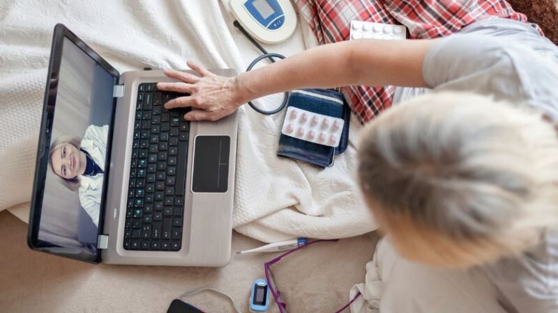Patiente âgée en téléconsultation médicale depuis son lit avec un médecin visible sur lécran de son ordinateur portable