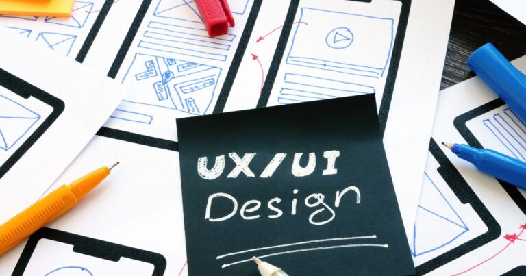 Feuilles de wireframes et carnet avec inscription UXUI Design entourés de stylos