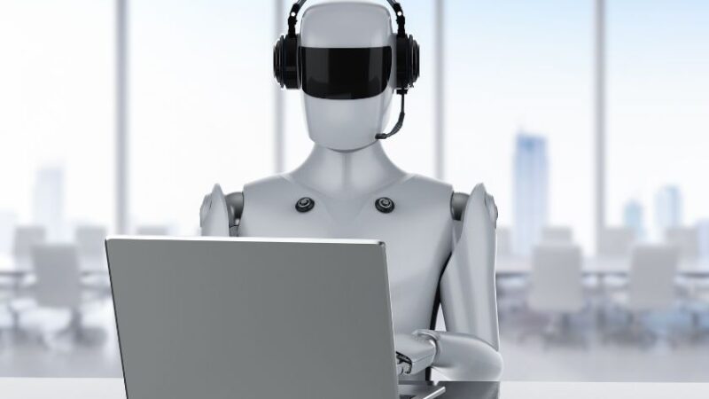 Robot humanoïde avec casque travaillant sur un ordinateur portable, illustrant l’automatisation du service client.