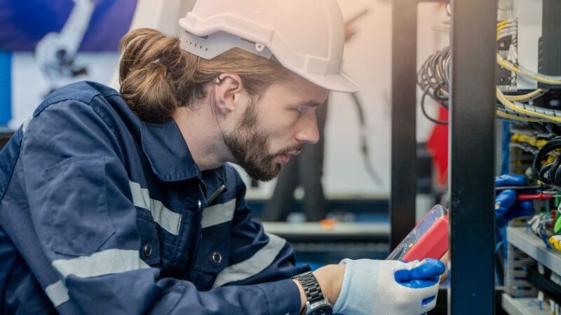 Technicien en tenue de travail et casque de sécurité effectuant un diagnostic sur un équipement informatique