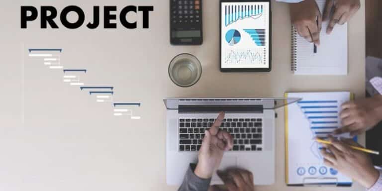 Vue de dessus dun poste de travail avec ordinateur portable tablette affichant des graphiques calculatrice et le mot PROJECT représentant la gestion de projet digital