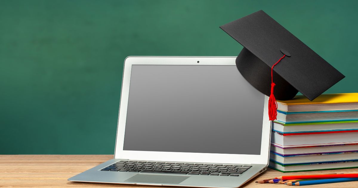 Ordinateur portable avec toque de diplômé posée sur une pile de livres symbolisant la réussite grâce à lapprentissage en ligne