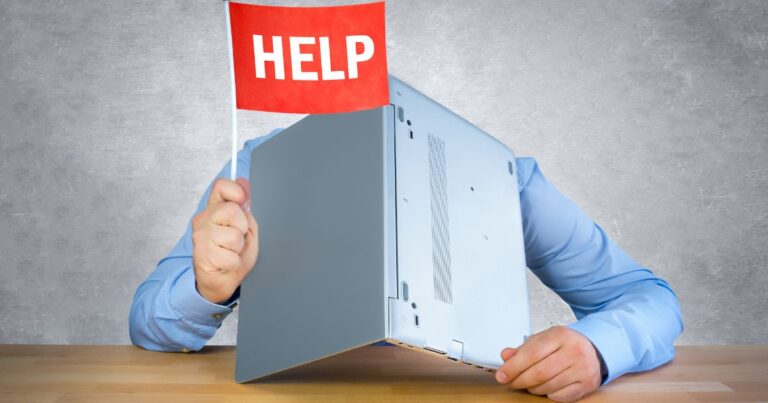 Personne cachée derrière un ordinateur portable en panne levant un drapeau rouge avec linscription HELP symbolisant une situation de détresse informatique