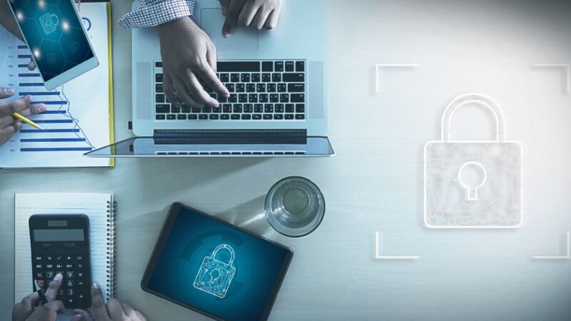 Équipe travaillant sur ordinateur portable et tablette avec icône de cadenas symbolisant la cybersécurité