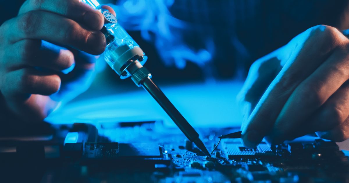 Gros plan sur des mains effectuant une soudure sur une carte mère avec un fer à souder illustrant la réparation et la maintenance informatique avancée