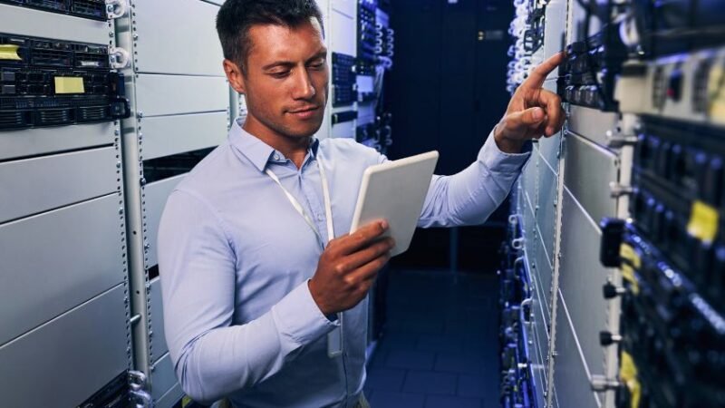 Technicien en centre de données inspectant des serveurs avec une tablette illustrant la maintenance préventive et la gestion dinfrastructure IT