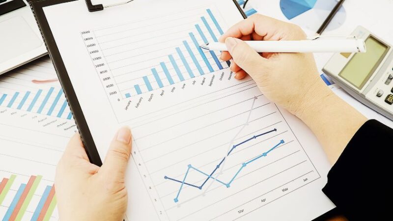 Personne analysant des graphiques financiers sur un tableau à pince avec un stylo