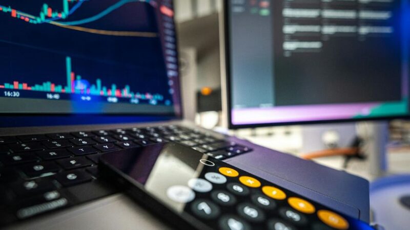 Écrans affichant des graphiques financiers sur ordinateur portable et moniteur avec calculatrice en premier plan