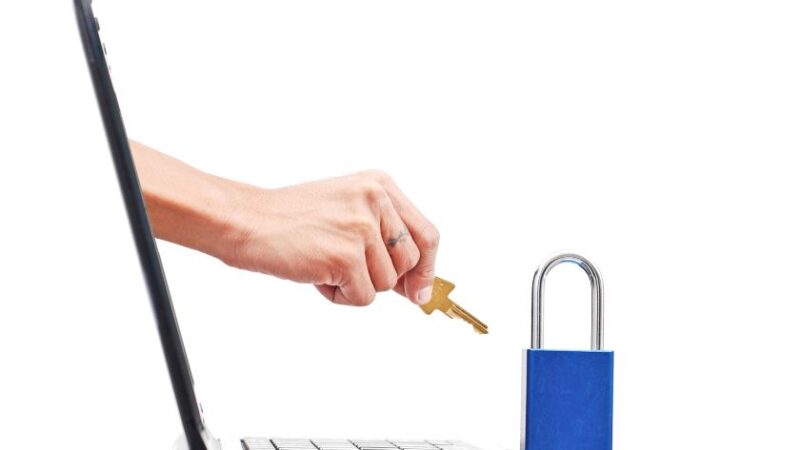 Main insérant une clé dans un cadenas posé sur un ordinateur portable symbolisant la cybersécurité et la protection des données numériques