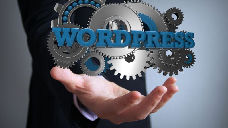 Main dun homme en costume tenant une structure de rouages métalliques avec le mot WordPress symbolisant les mécanismes internes du CMS
