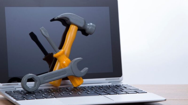 Ordinateur portable avec outils de maintenance posés dessus clé tournevis marteau symbolisant la réparation ou loptimisation informatique