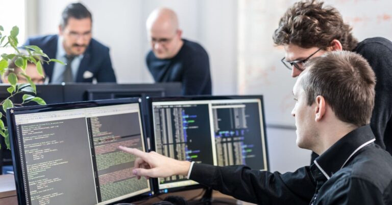 Équipe de développeurs collaborant devant plusieurs écrans affichant du code informatique dans un bureau moderne